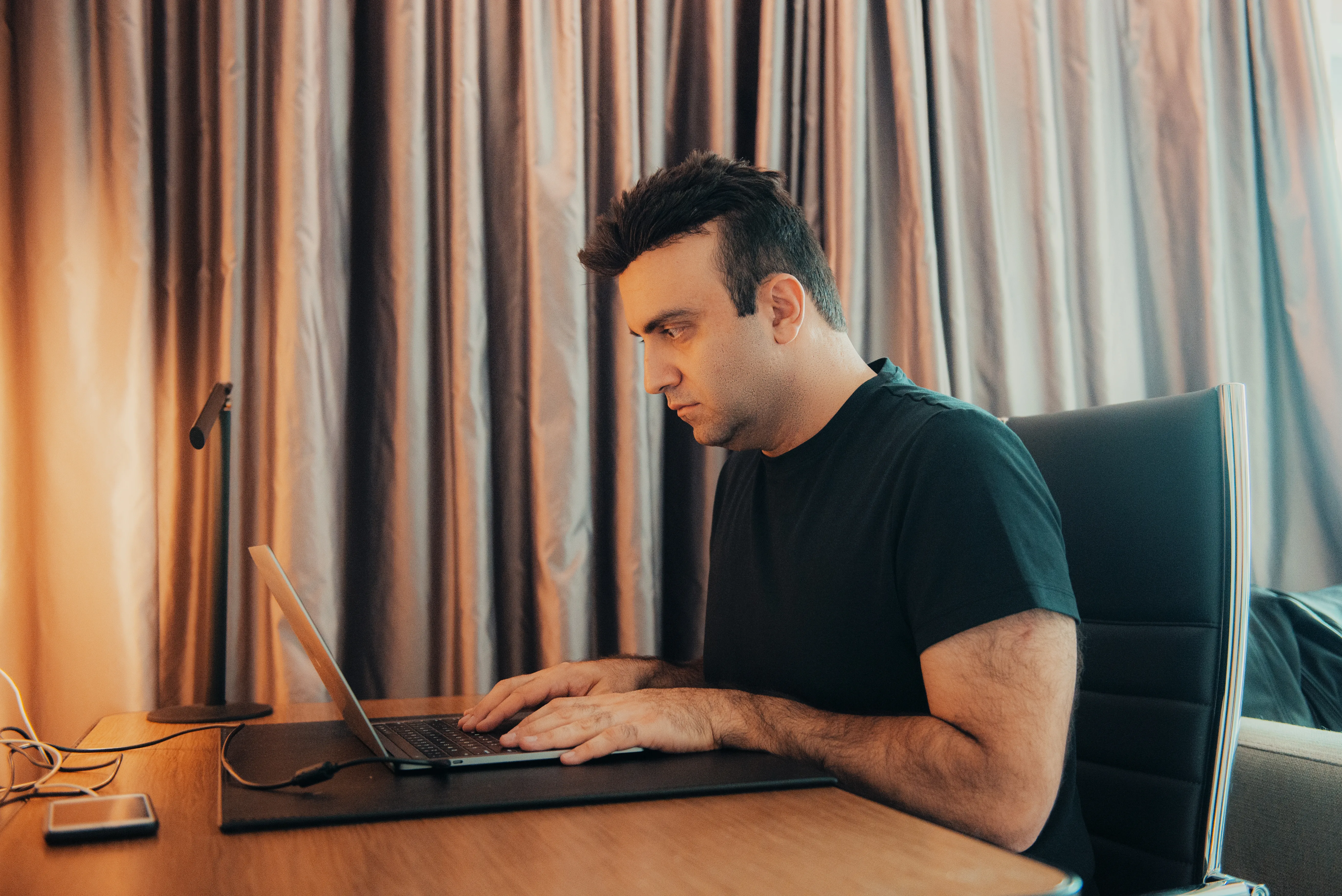Taha Asadi at his desk, focused on a laptop in warm lamplight