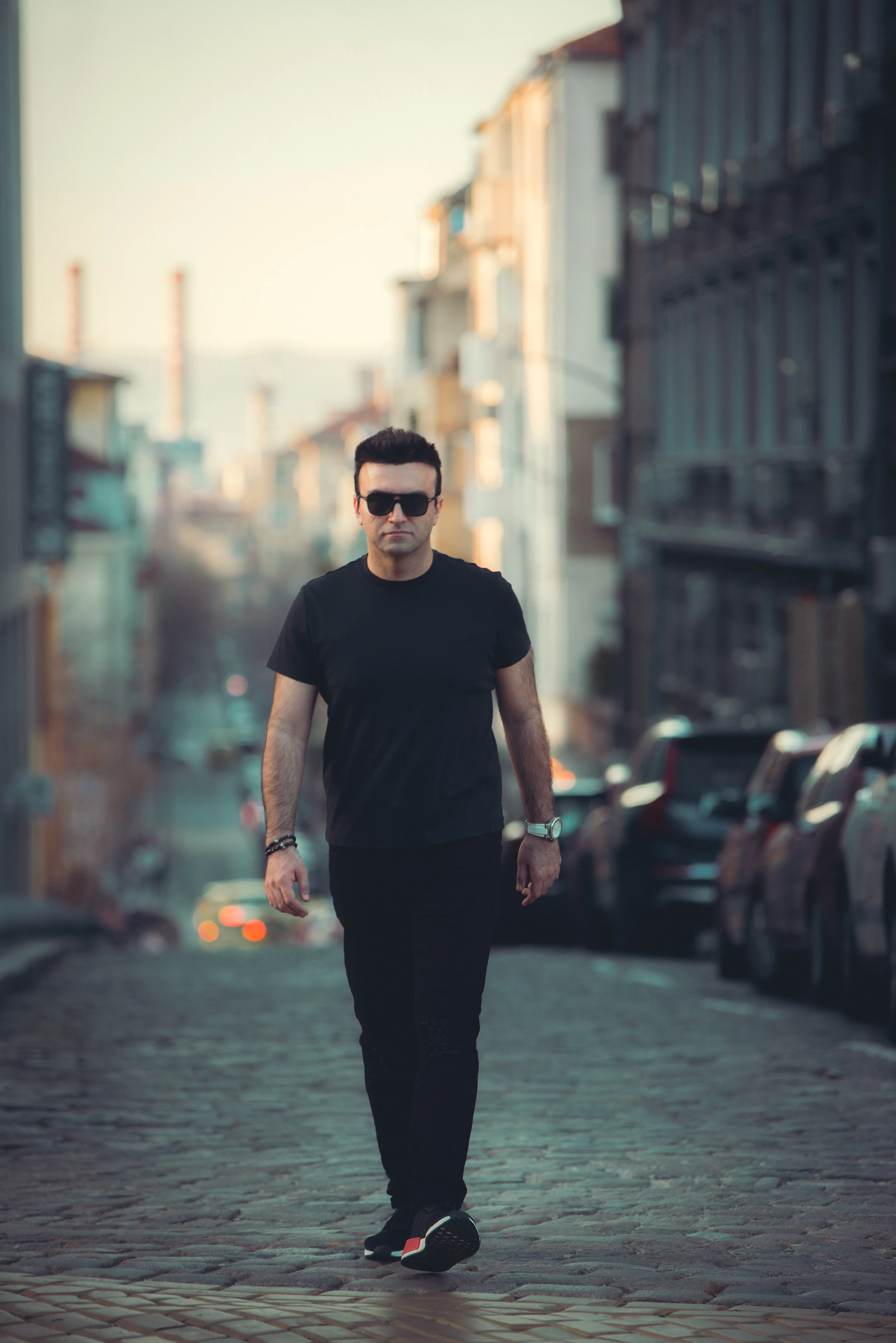 Taha Asadi in sunglasses walking down a cobblestone street lined with parked cars