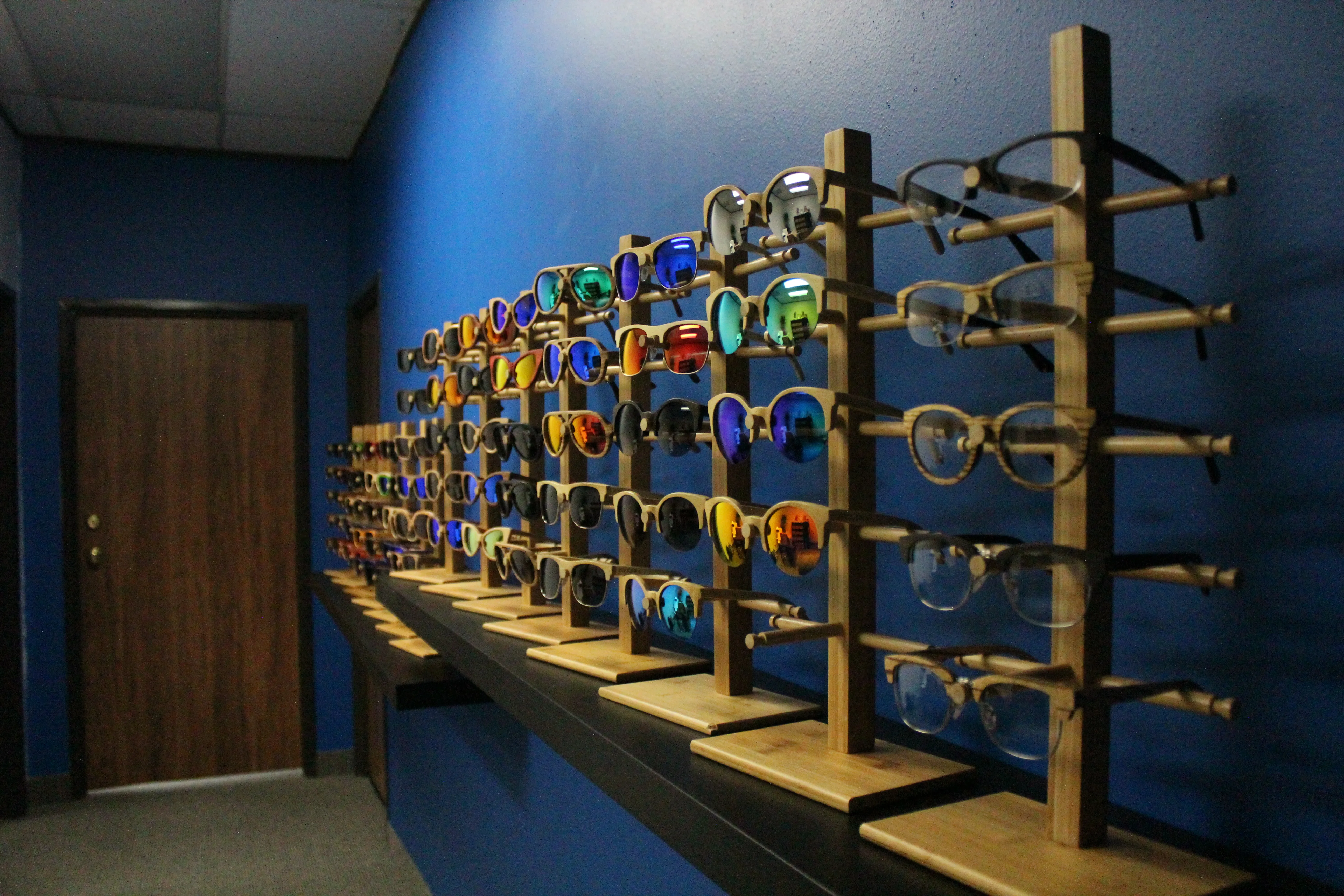 Zylina retail display wall: rows of wooden sunglasses and eyewear on bamboo racks against a blue wall